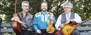 The Doc Wallace Trio (David Wallace, Fiddle; Daniel Levy, guitar; Dana Scofidio, electric guitar) sitting on a bench in Fort Tryon Park