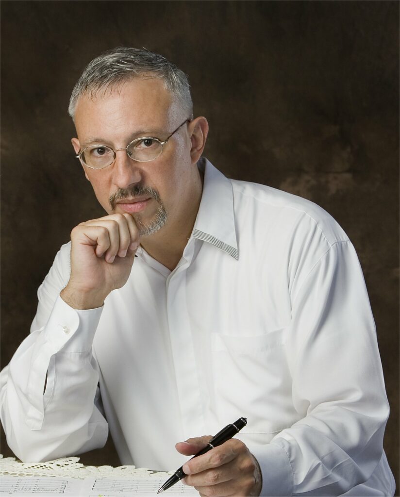 This image is a publicity photo of composer Miguel del Águila wearing a white shirt, holding a pencil, writing onto a score of staff paper. Miguel's piece "Submerged" is the subject of Dr. David Wallace's Journal of the American Viola Society Article "Let's Play Submerged!"